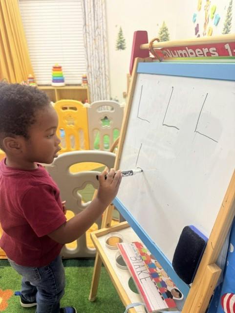 Child using a marker to write on a whiteboard in a playroom