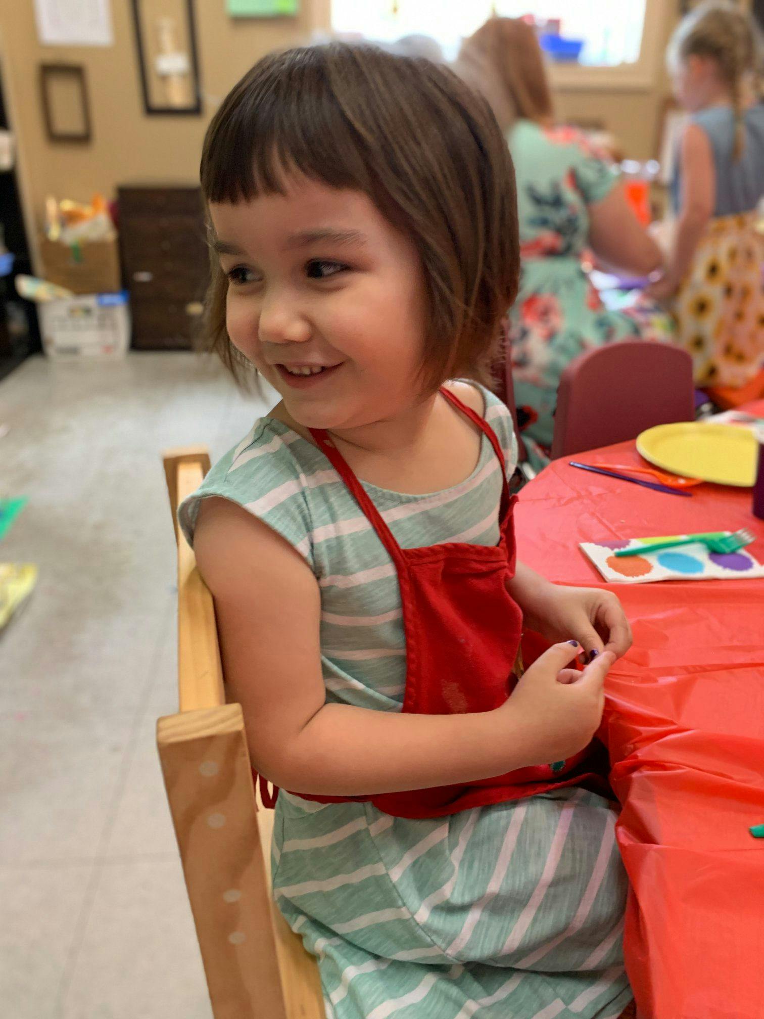 Child in a red apron sitting at a table
