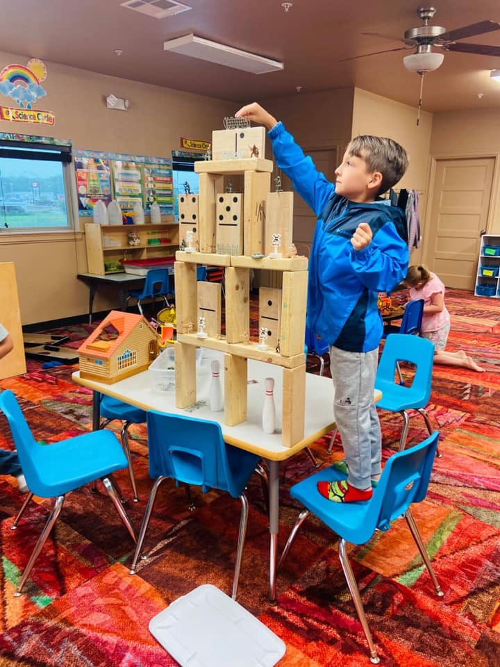 Child standing on a chair building a tower with wooden blocks