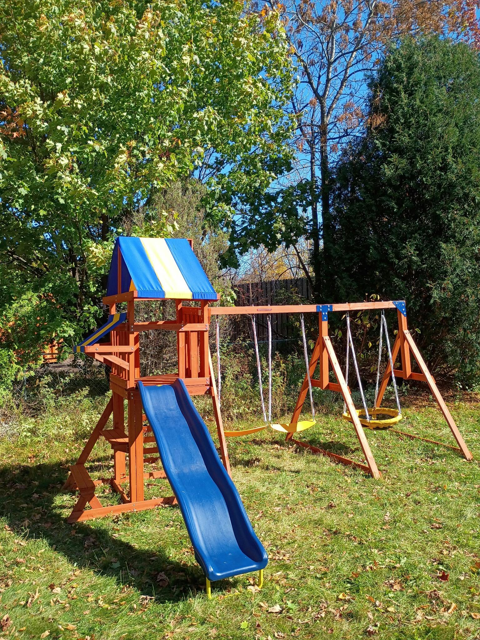 Wooden playset with a slide and swings in a grassy yard
