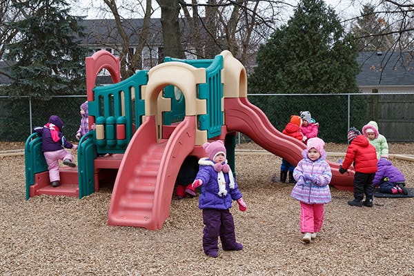 Children playing on a playground structure with a slide and climbing structure
