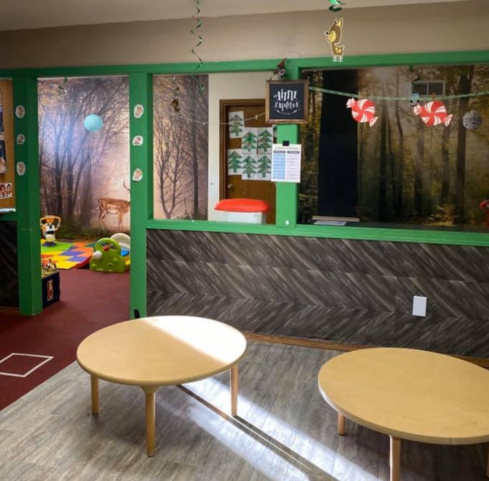 Two small round tables in a room with a forest-themed play area