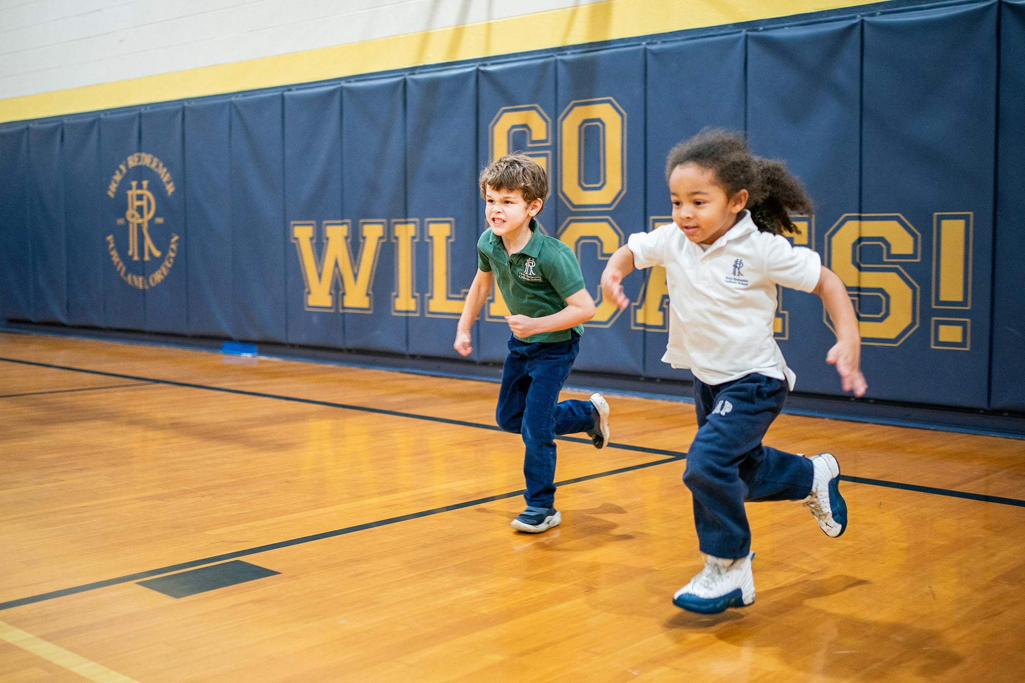 Two children running on a wooden floor in a gym