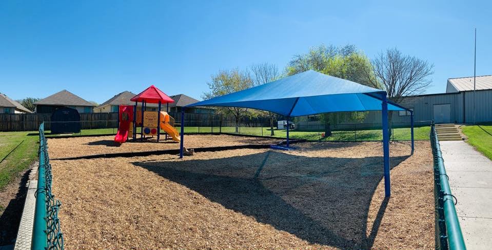 Playground with a red and yellow play structure and a blue shade canopy
