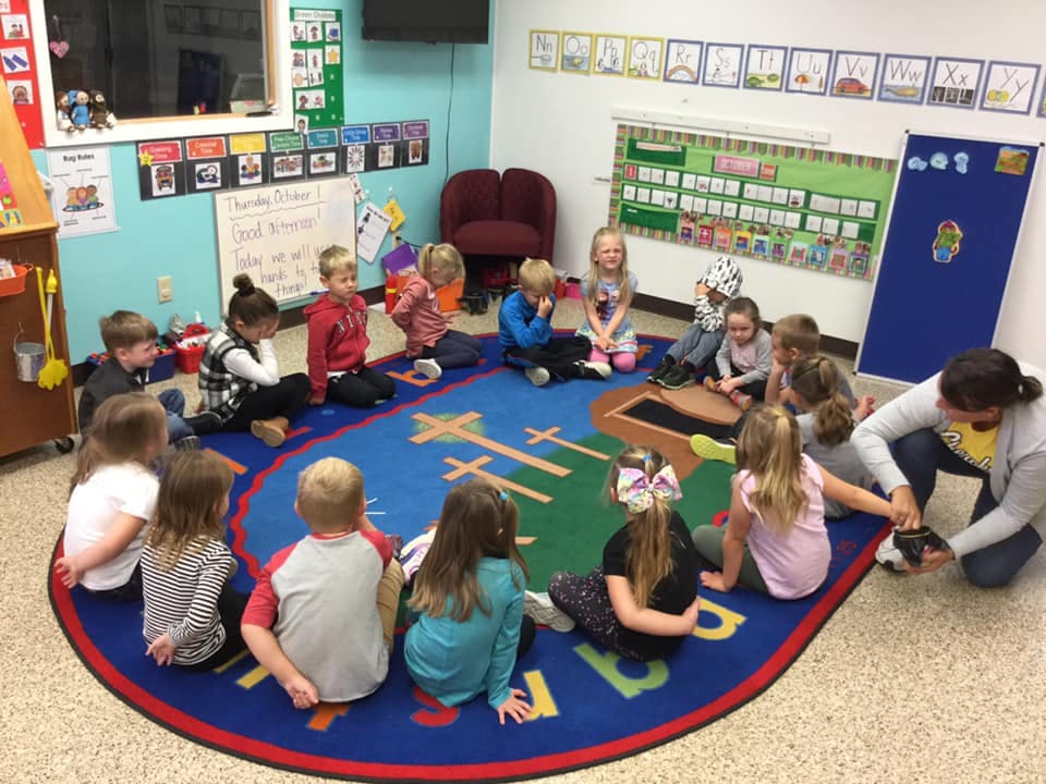 Children sitting on a rug in a classroom with an adult