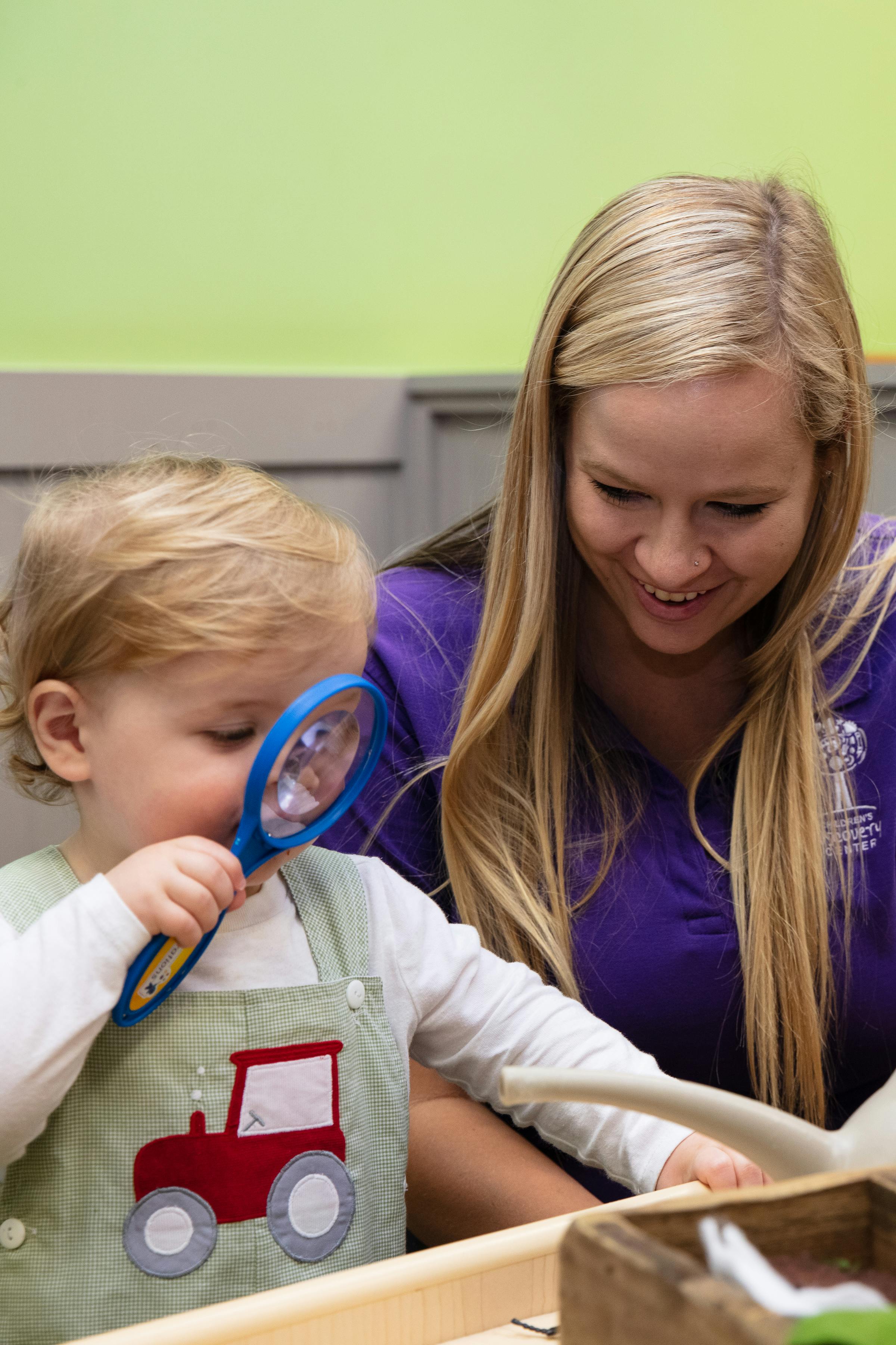 Child looking through a magnifying glass with an adult nearby