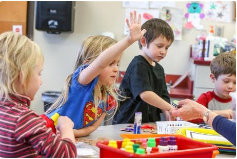 Child in a blue shirt raising a hand in a classroom