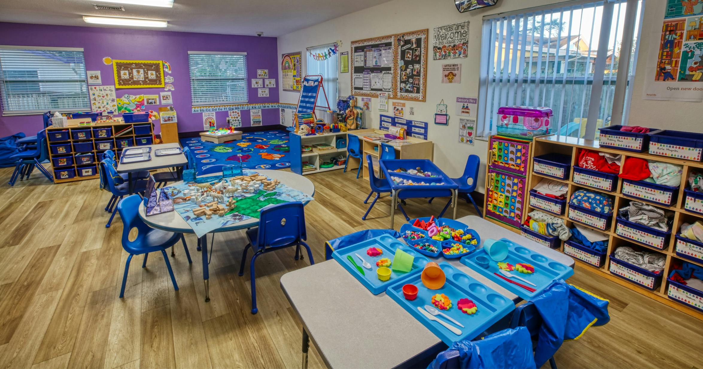 Classroom with small tables and chairs, shelves with toys and materials, and colorful decorations