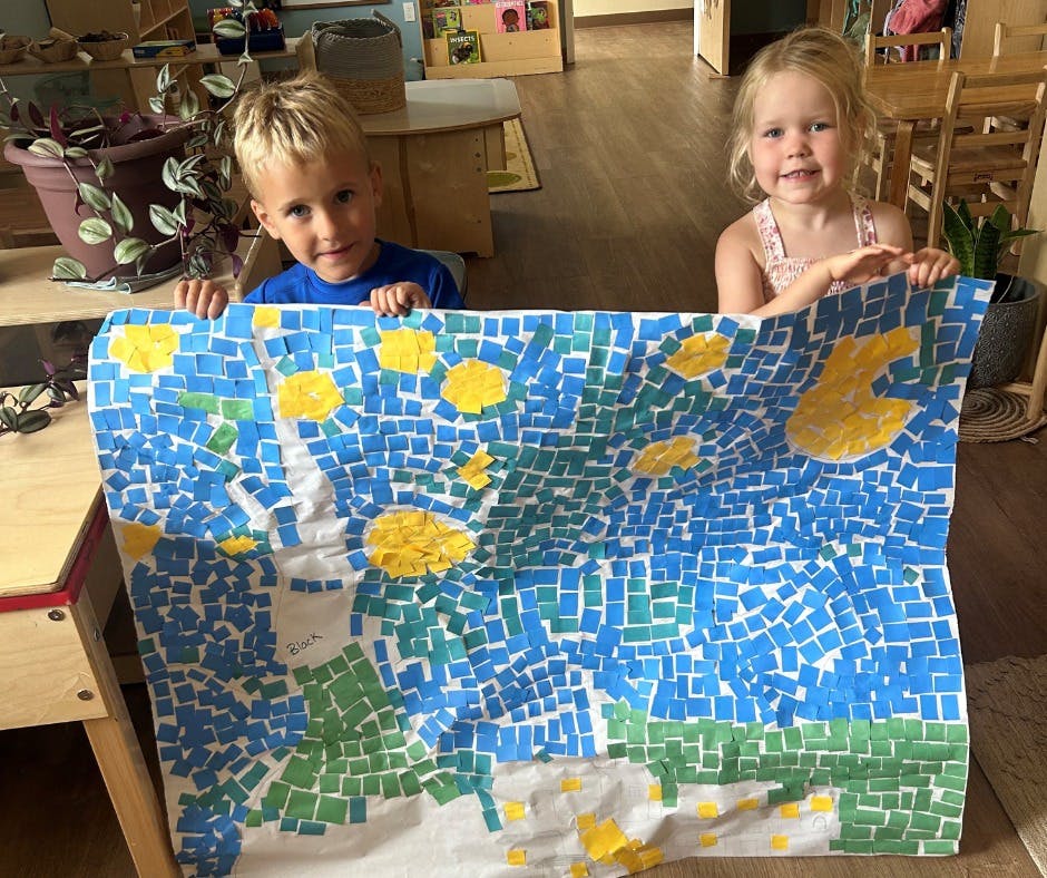 Two children holding up a large mosaic art project