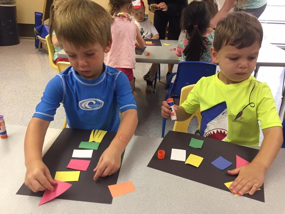 Two children doing crafts with paper shapes and glue sticks