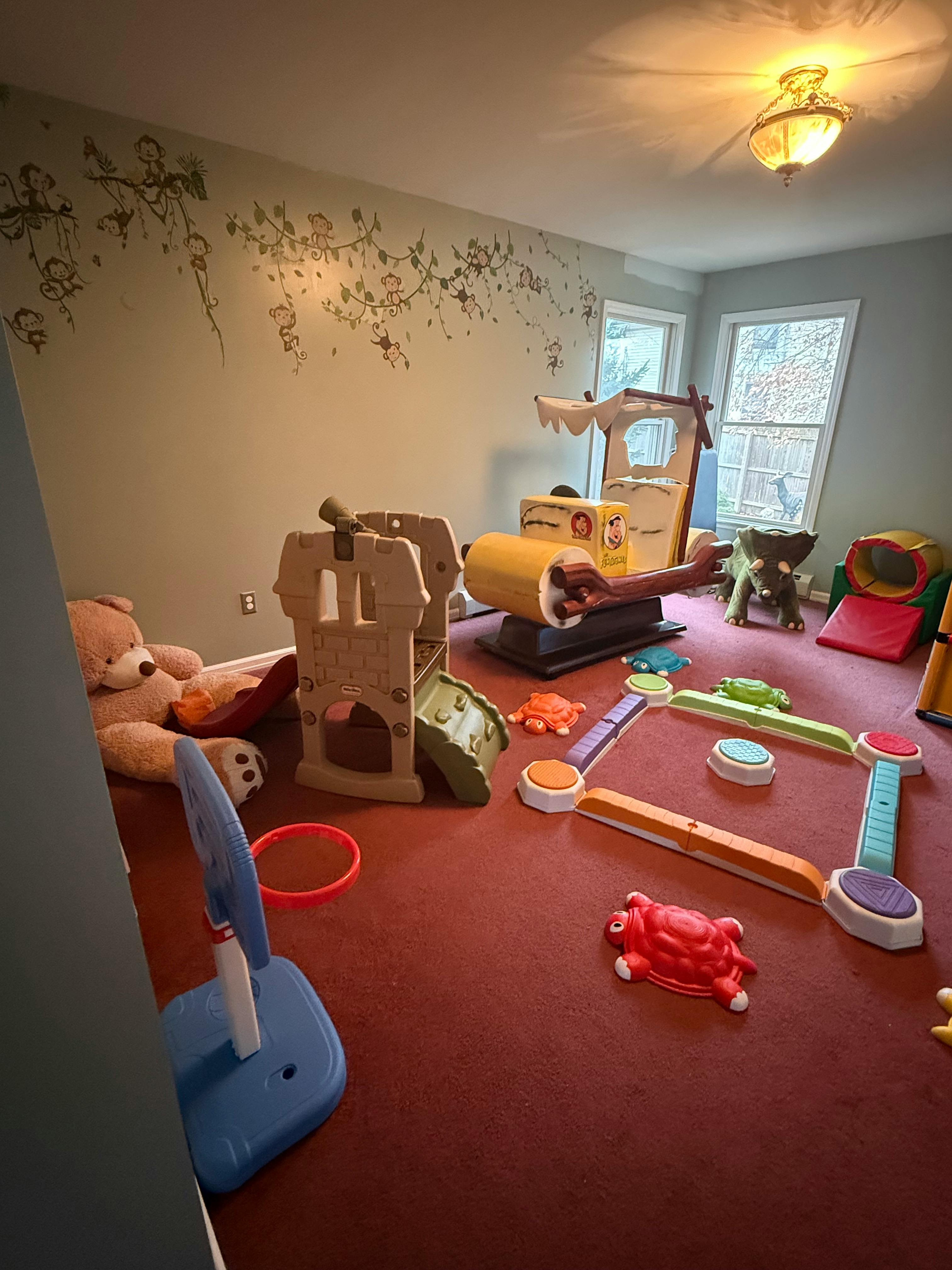 Playroom with various toys including a large teddy bear, play structure, and ride-on toy