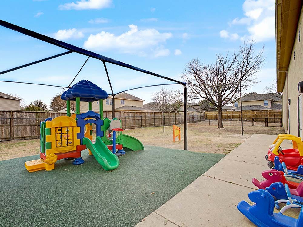 Colorful outdoor playground with slides and ride-on toys under a shade canopy