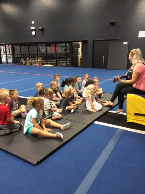 Person playing guitar for a group of children sitting on mats