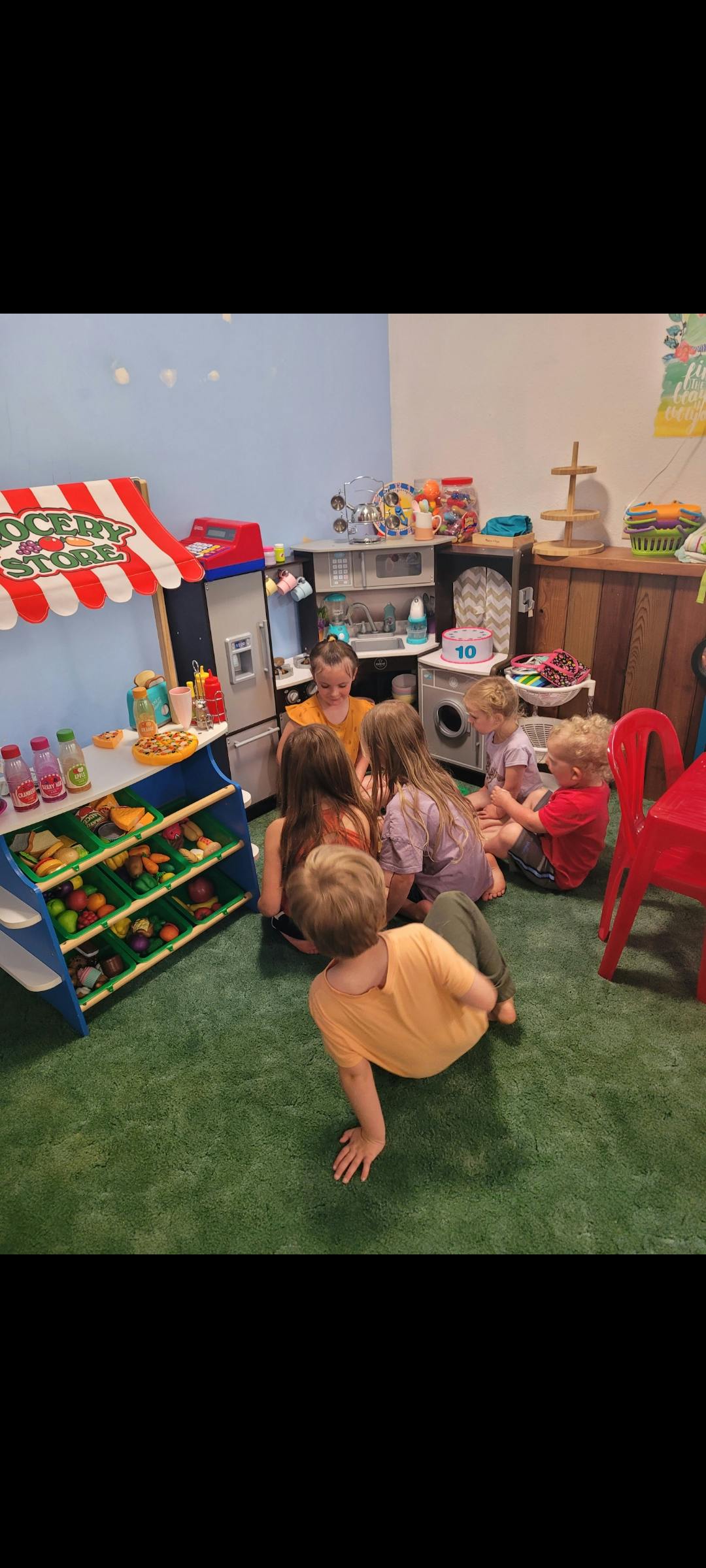 Children playing on the floor in a room with toy kitchen and grocery store