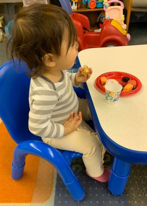 Child sitting at a table with a plate of fruit and a cup