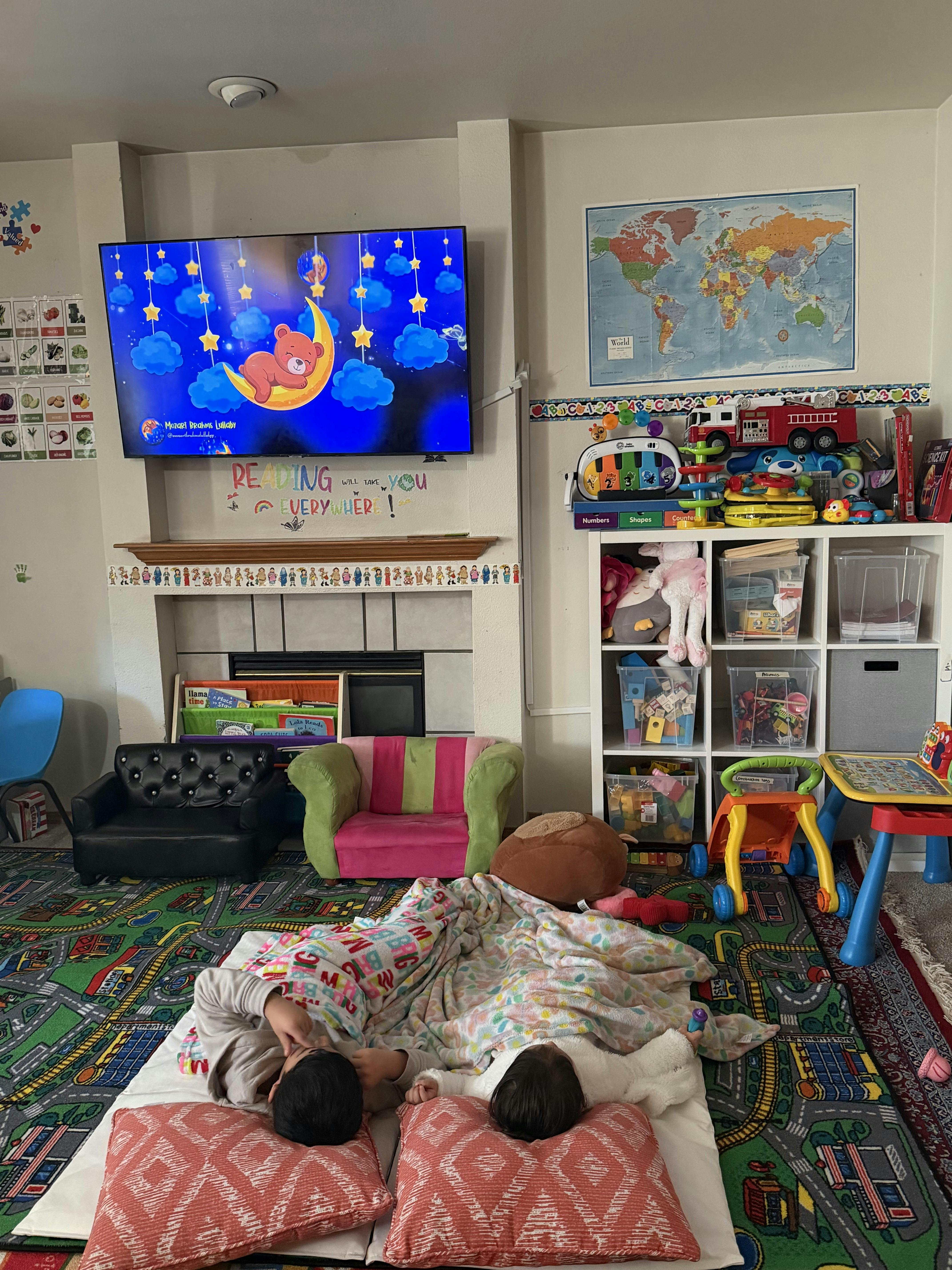 two children lying on floor with blankets, watching a cartoon on TV