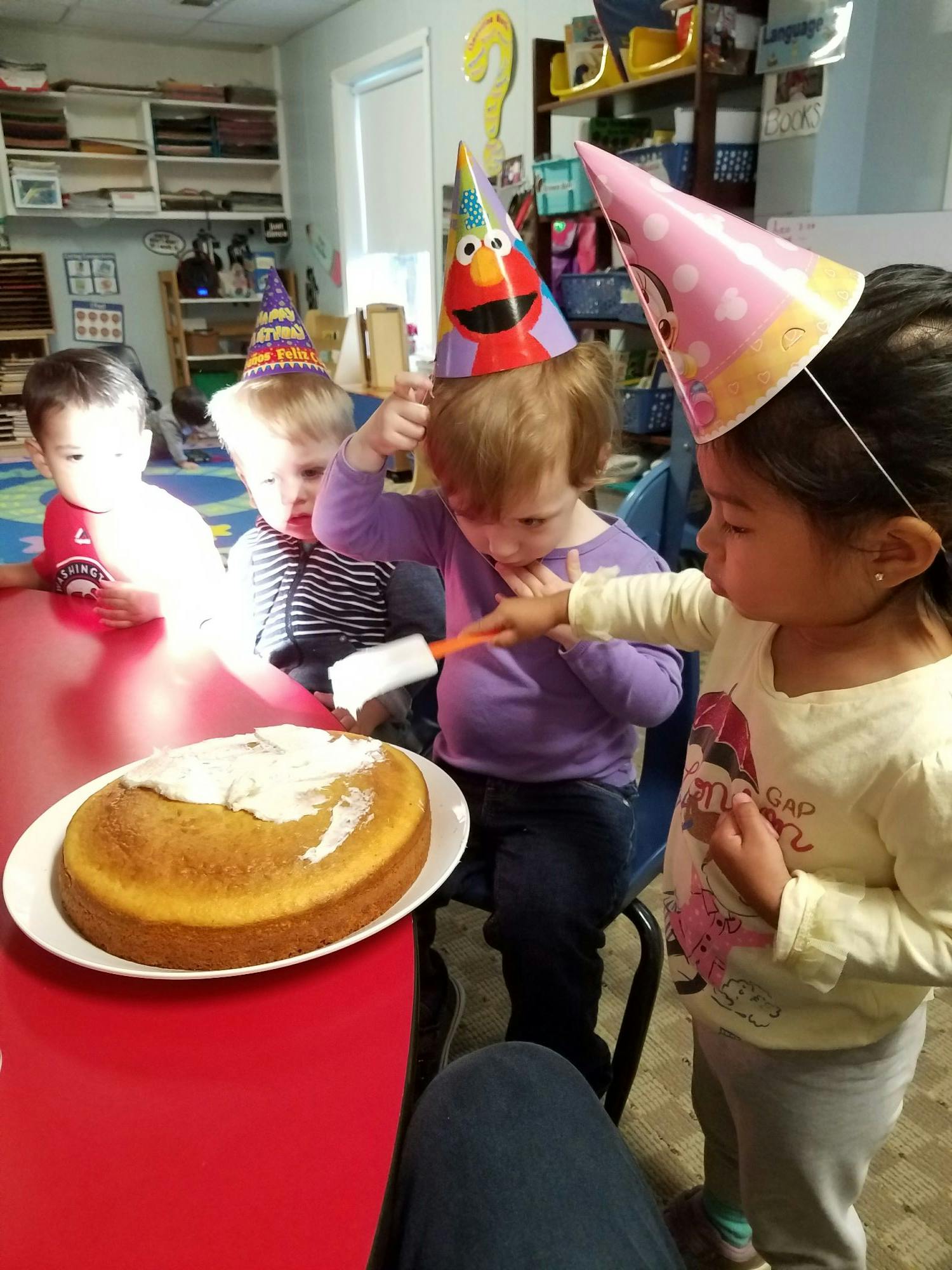 Children in party hats decorating a cake