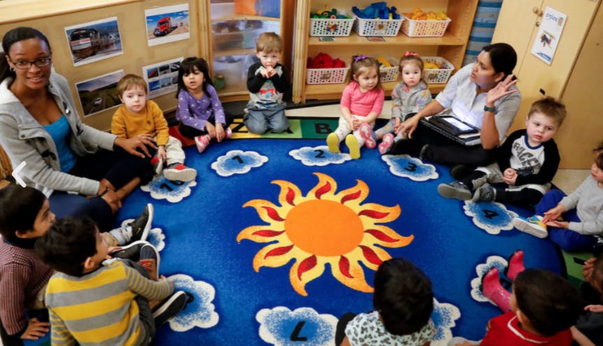 Two people and multiple children sitting on a sun-patterned rug