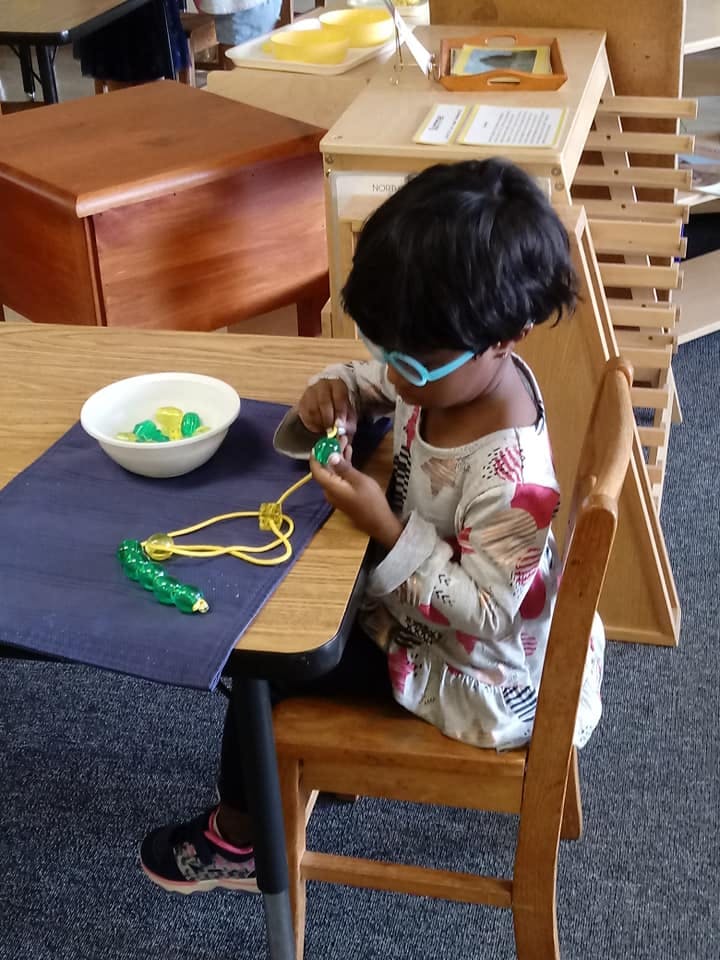 Child with glasses sitting at a table, stringing beads