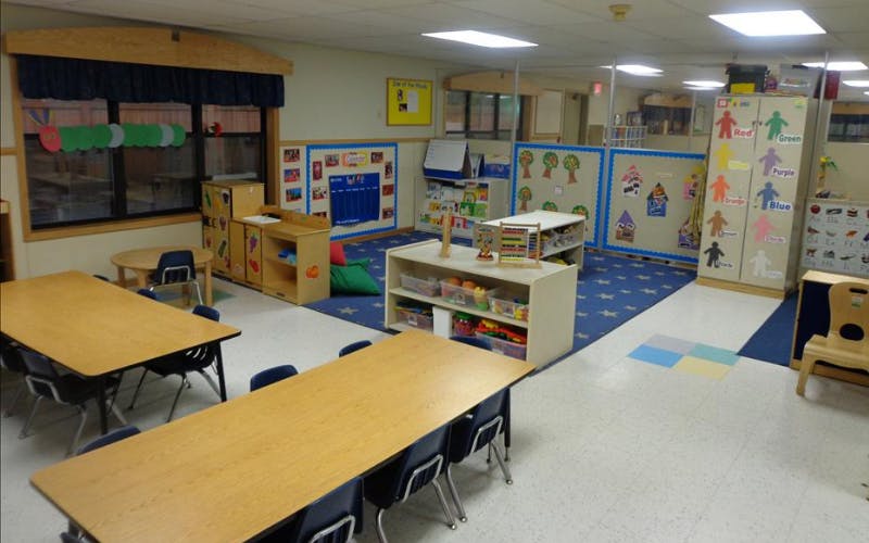 Empty classroom with small tables and chairs, toys on shelves, and colorful wall decorations