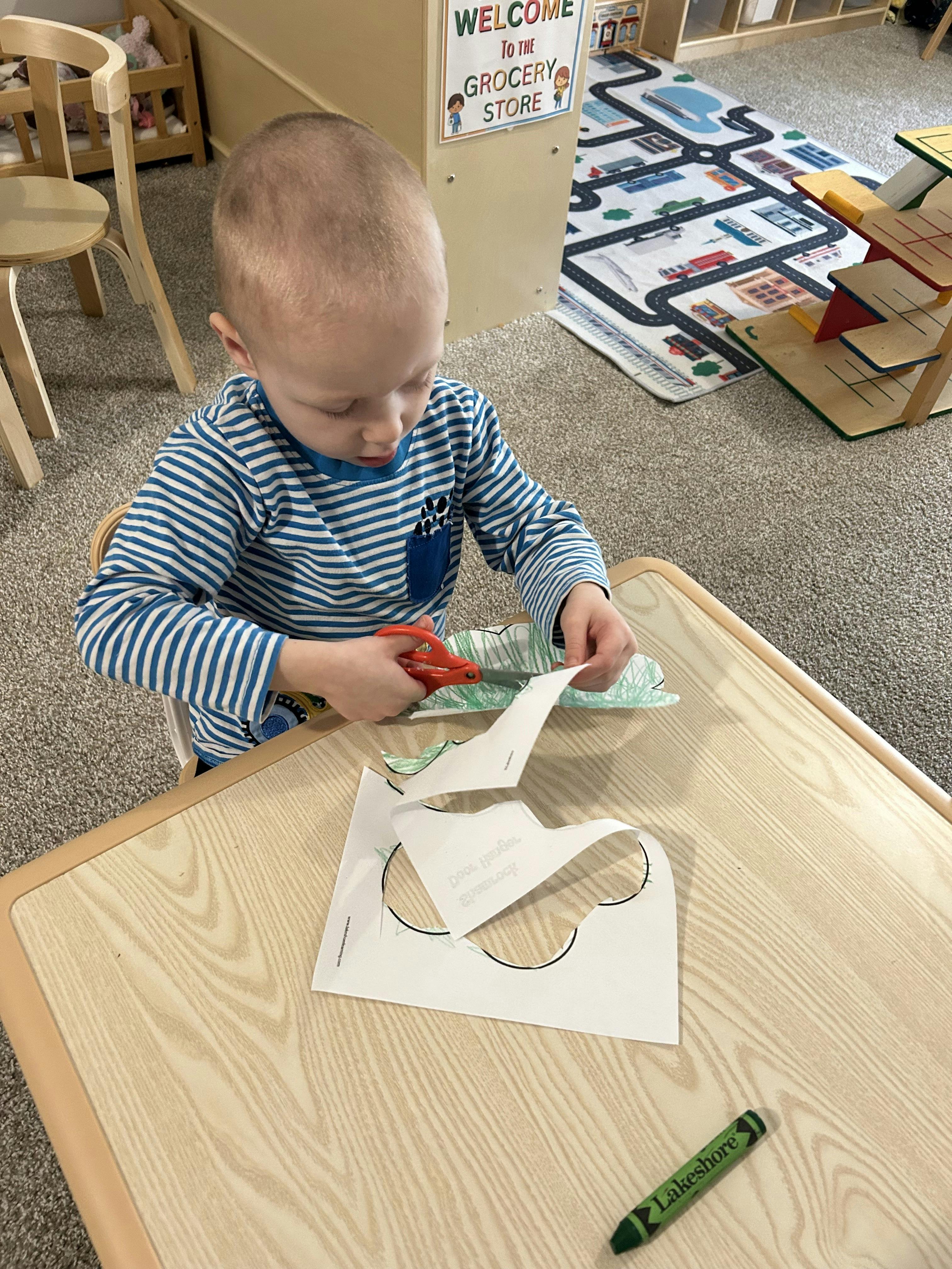 Child sitting at a table cutting paper with scissors