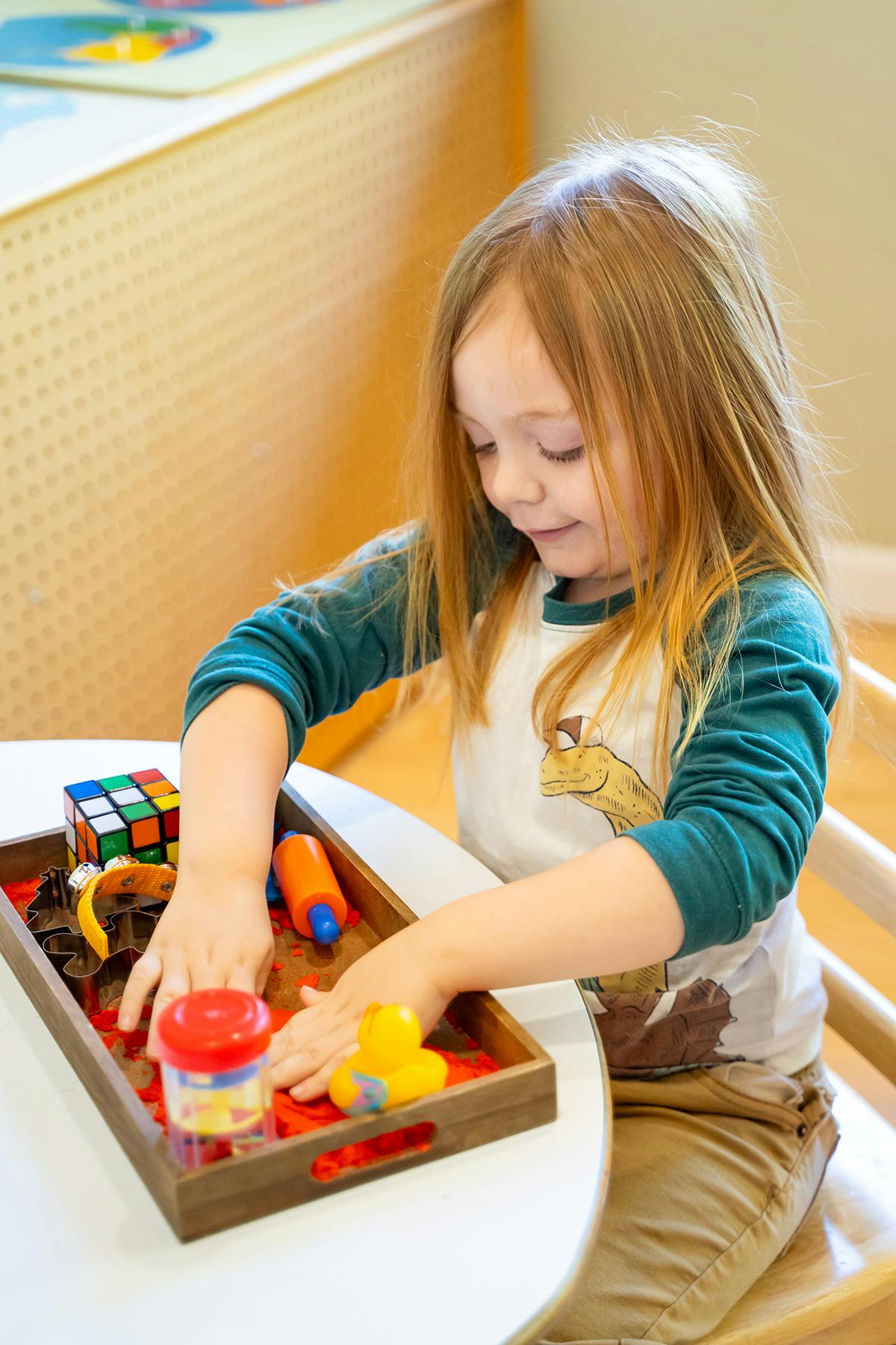 Child playing with toys in a wooden tray