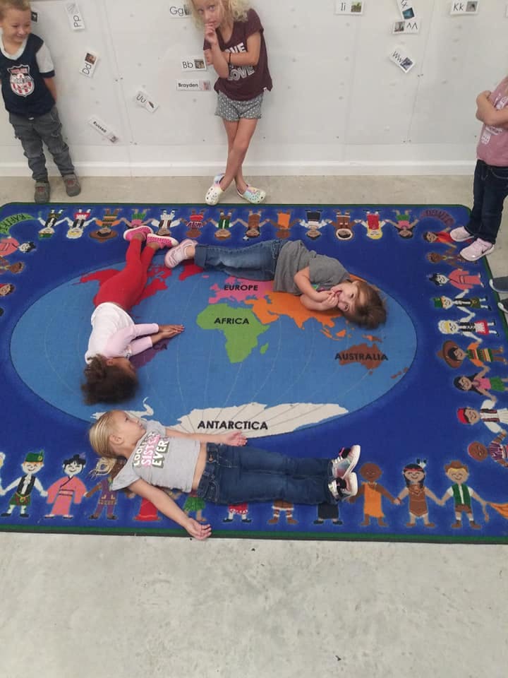 Children lying on a world map rug in a classroom