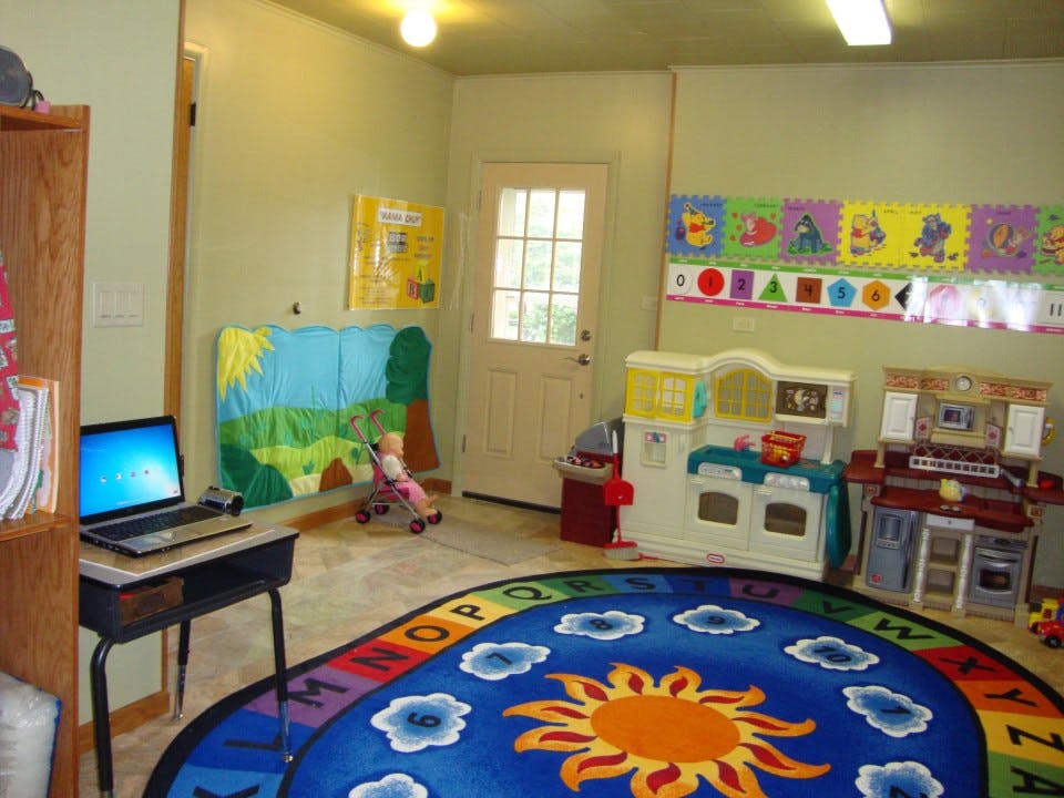 Playroom with a sun and alphabet rug, toy kitchen, and laptop on a desk