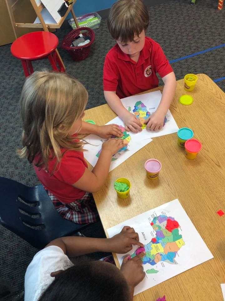 Three children playing with colorful clay on paper maps at a table