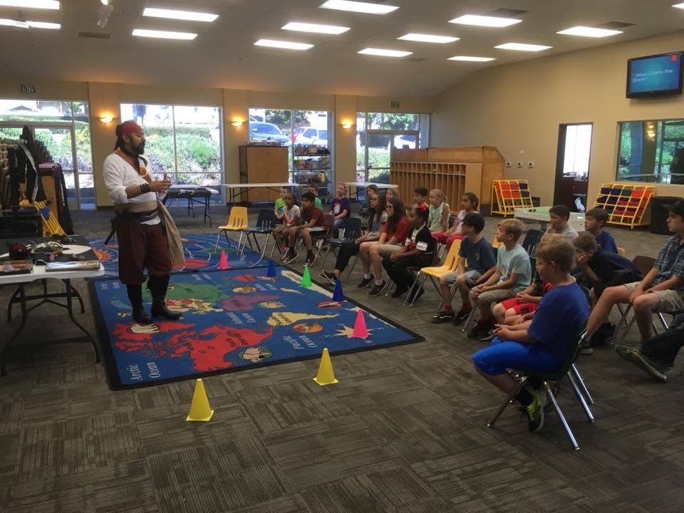 Person in pirate costume speaking to children seated on chairs