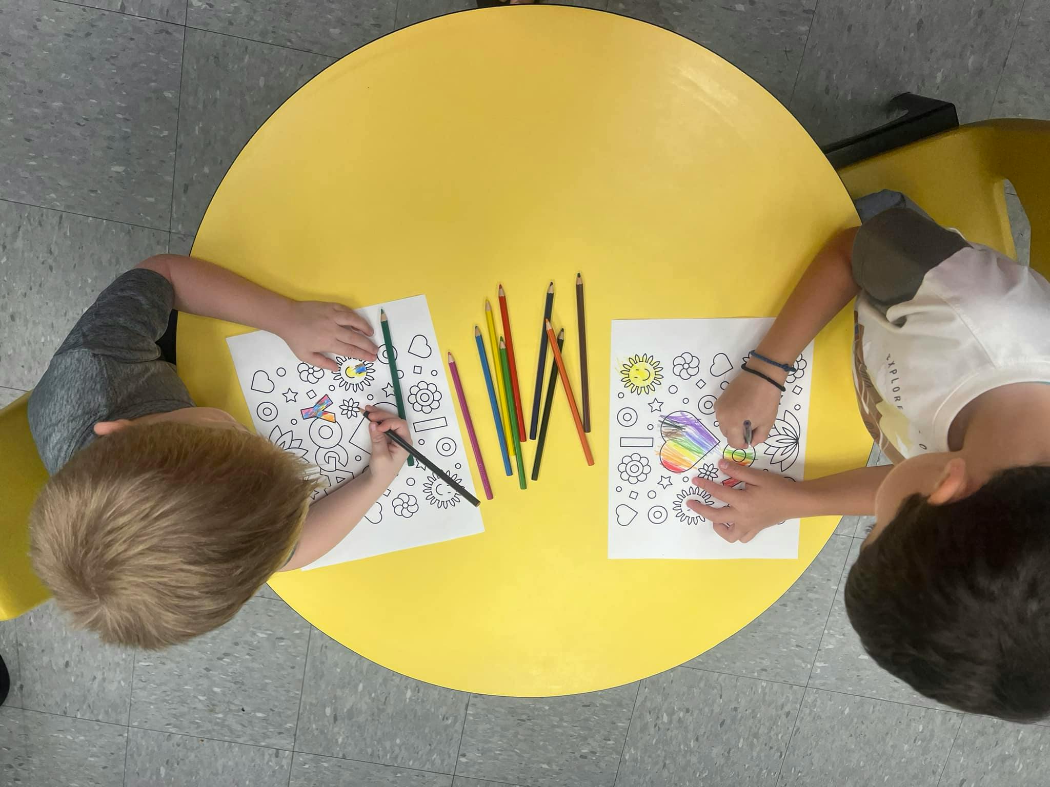 Two children coloring at a yellow table
