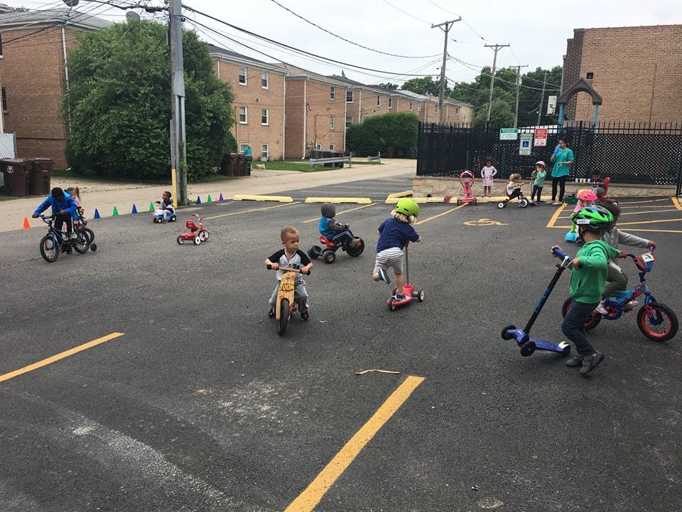 Children riding bikes, scooters, and tricycles on pavement