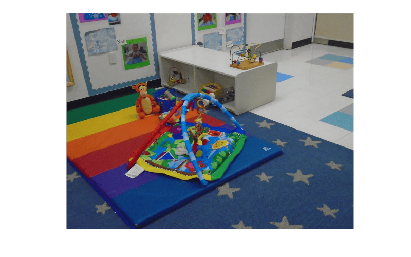 A baby playmat with toys on a rainbow mat in a classroom