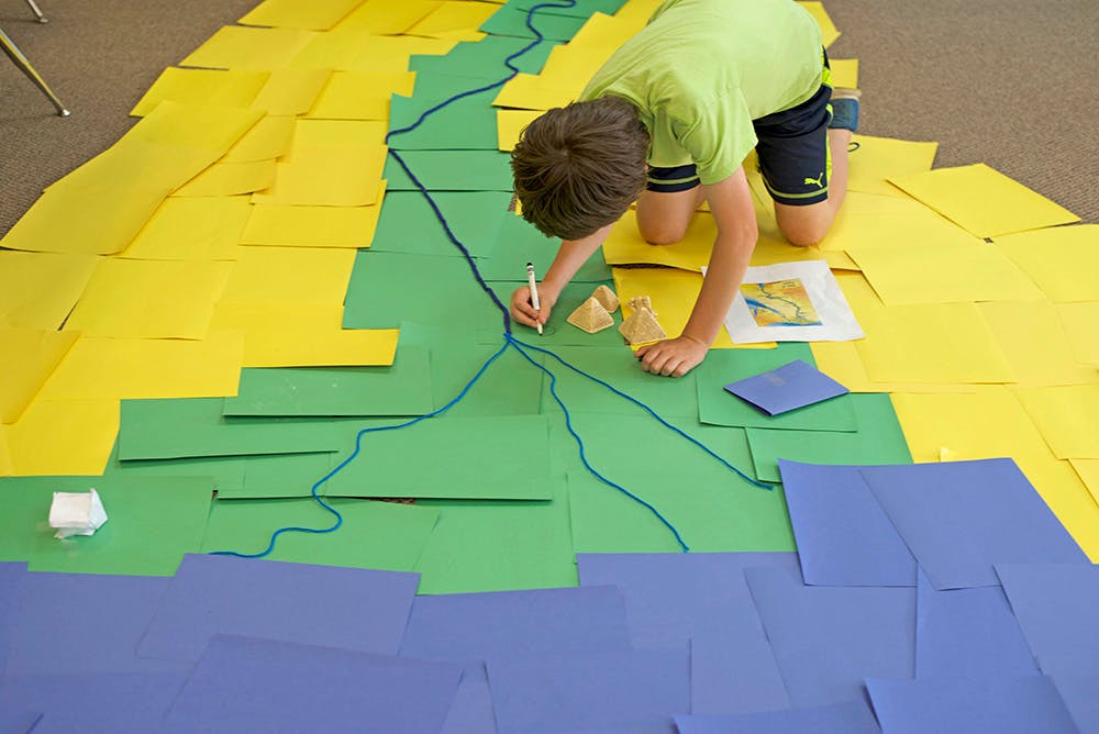 Child drawing on a large paper map on the floor
