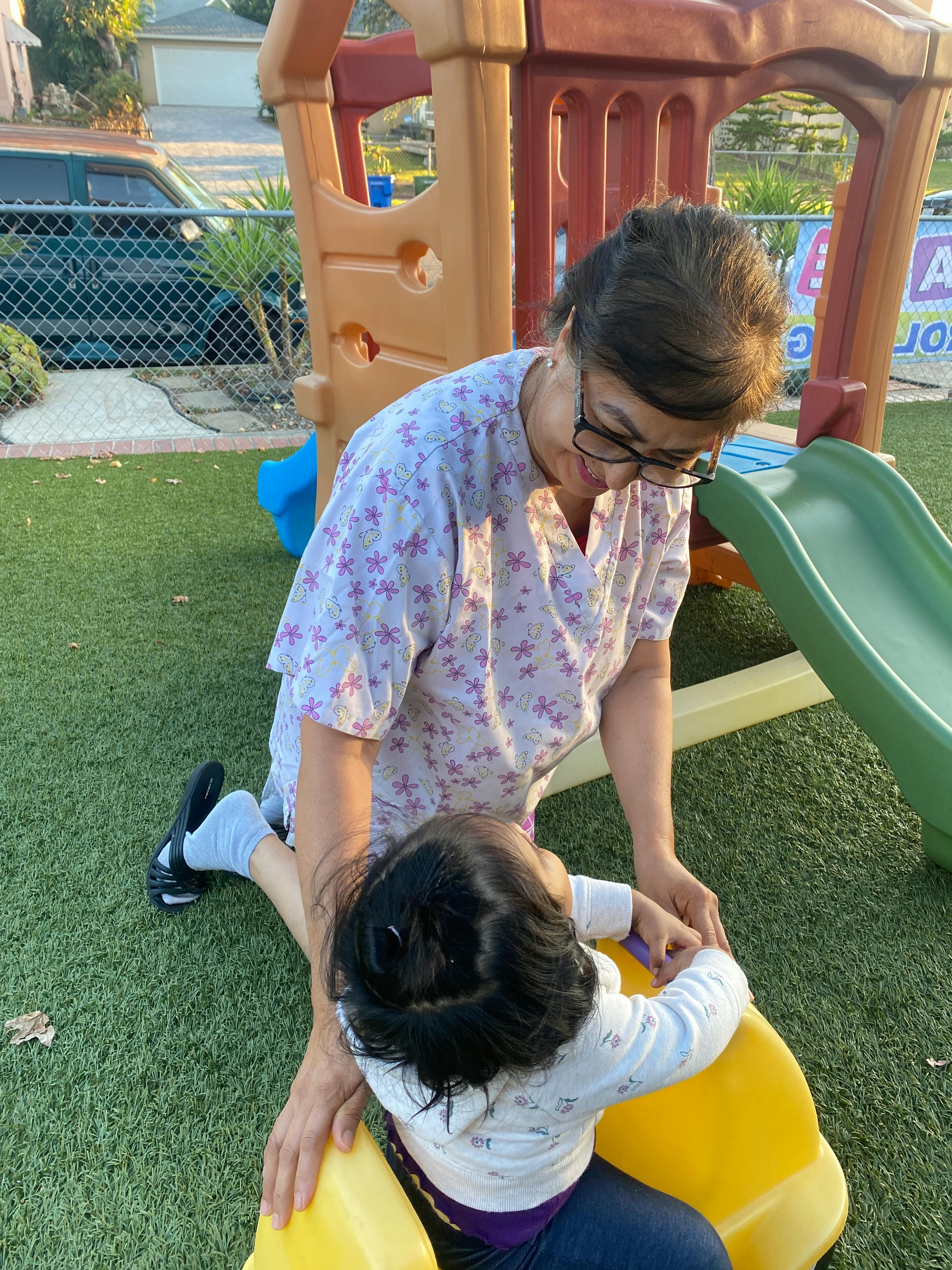 Person kneeling on grass with a child on a yellow toy