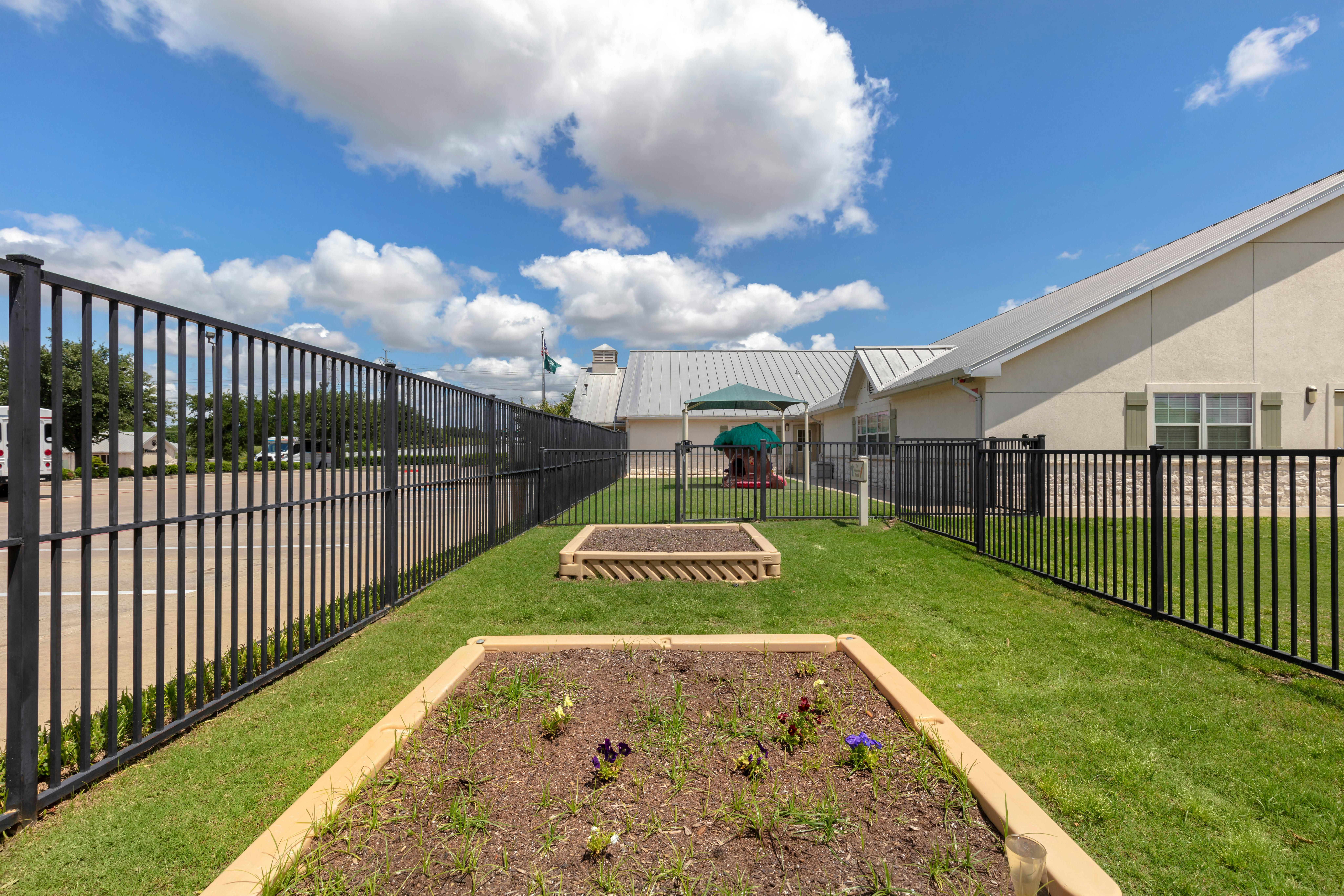 Fenced yard with two garden beds, green grass, and a building with a metal roof