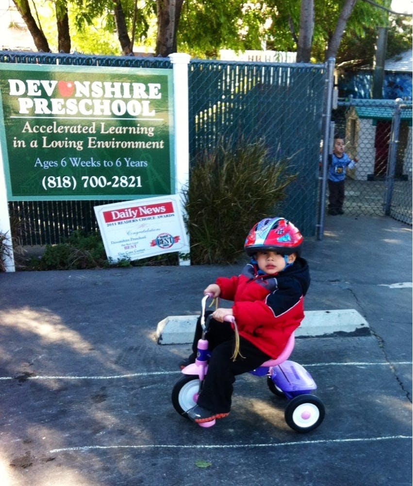 Child in a helmet on a tricycle near a preschool sign
