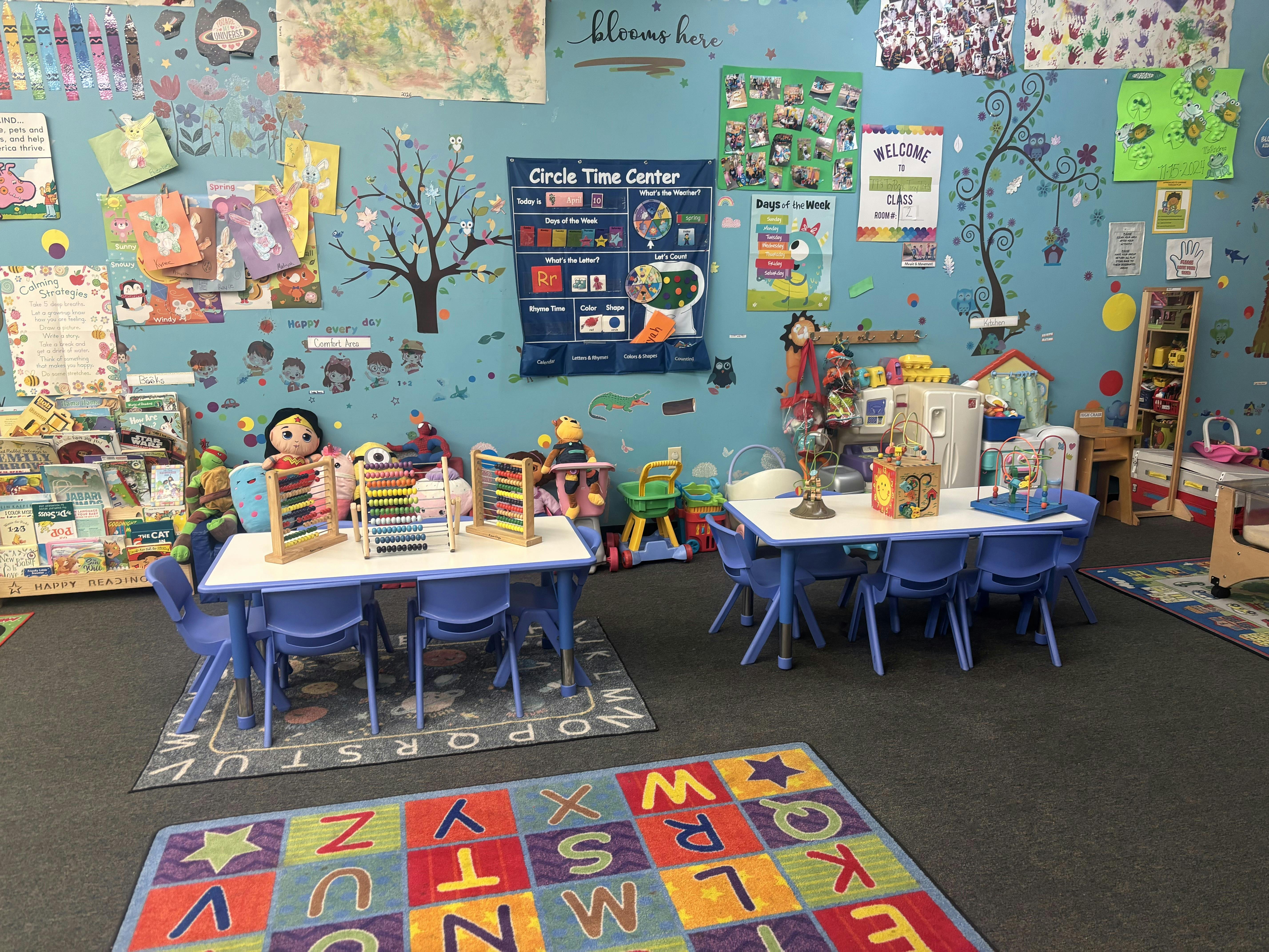 A classroom with blue walls decorated with cutouts, child-sized tables and chairs