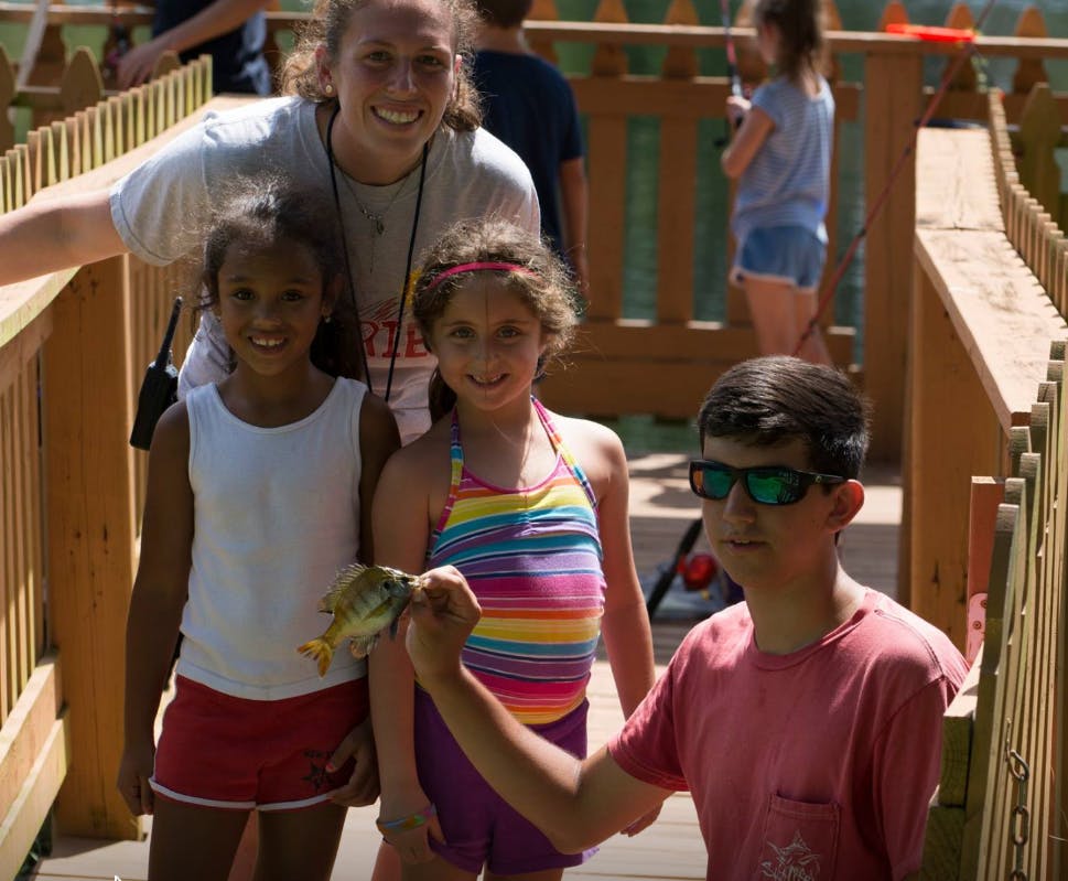 Person and three children on a wooden walkway, one child holding a small fish