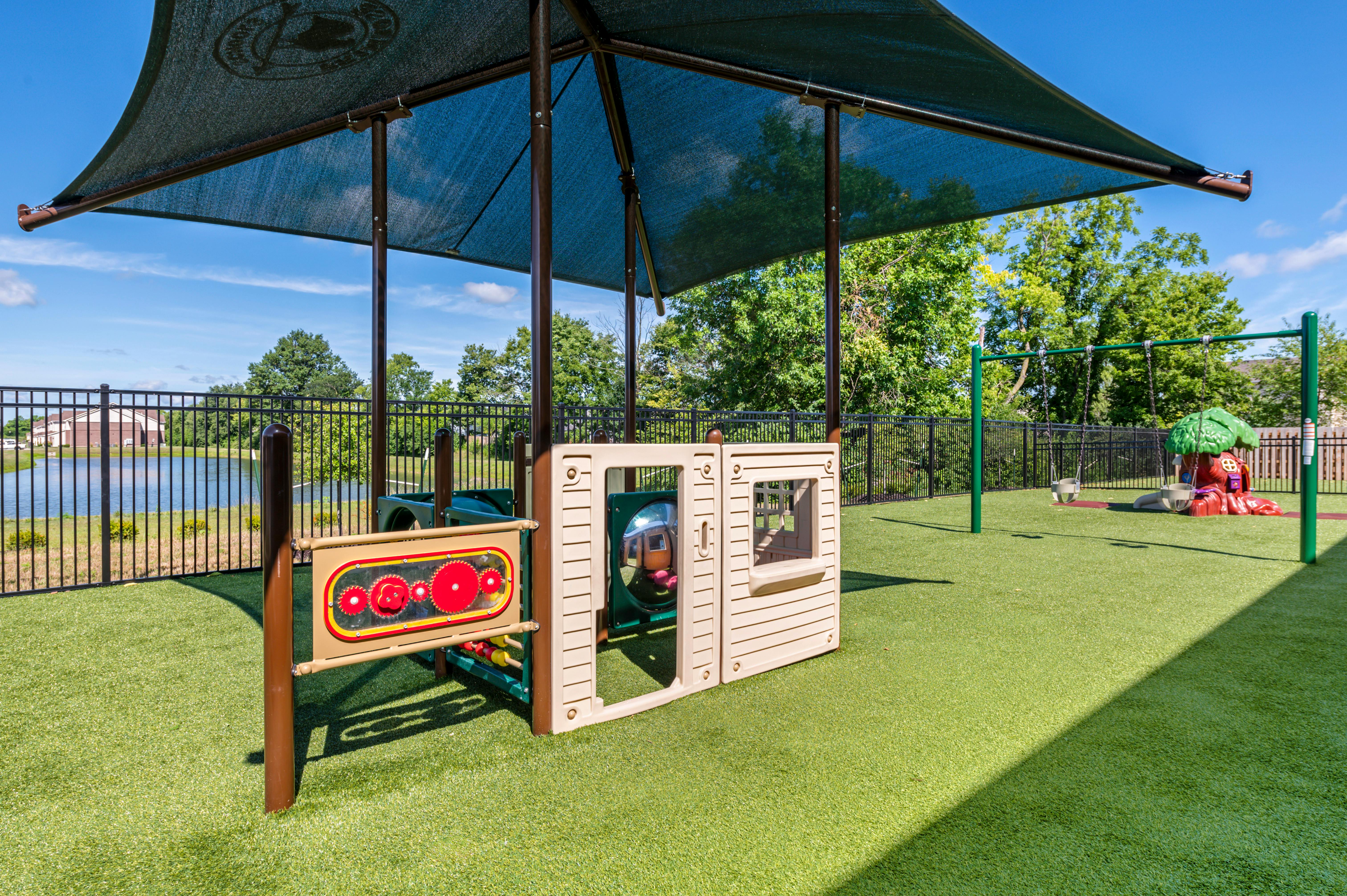 Playground area with various equipment on artificial turf under a shade canopy