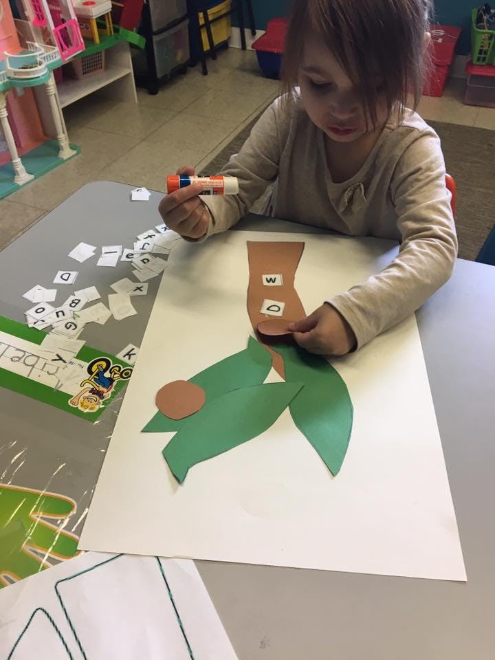 Child gluing paper letters onto a paper cutout