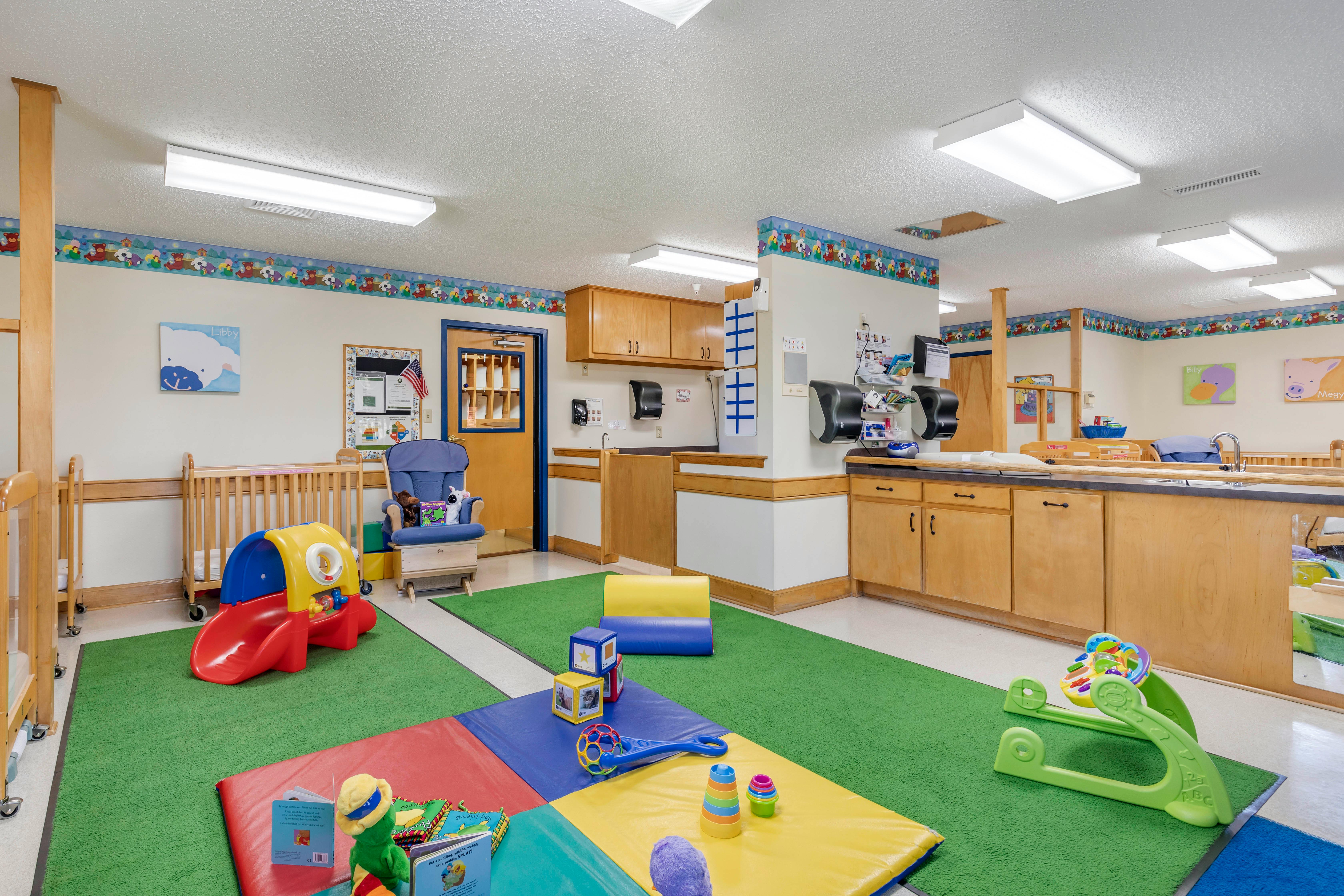 A colorful childcare room with cribs, play equipment, and changing stations
