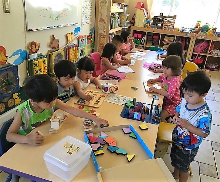 Children playing with puzzles and blocks at tables in a classroom