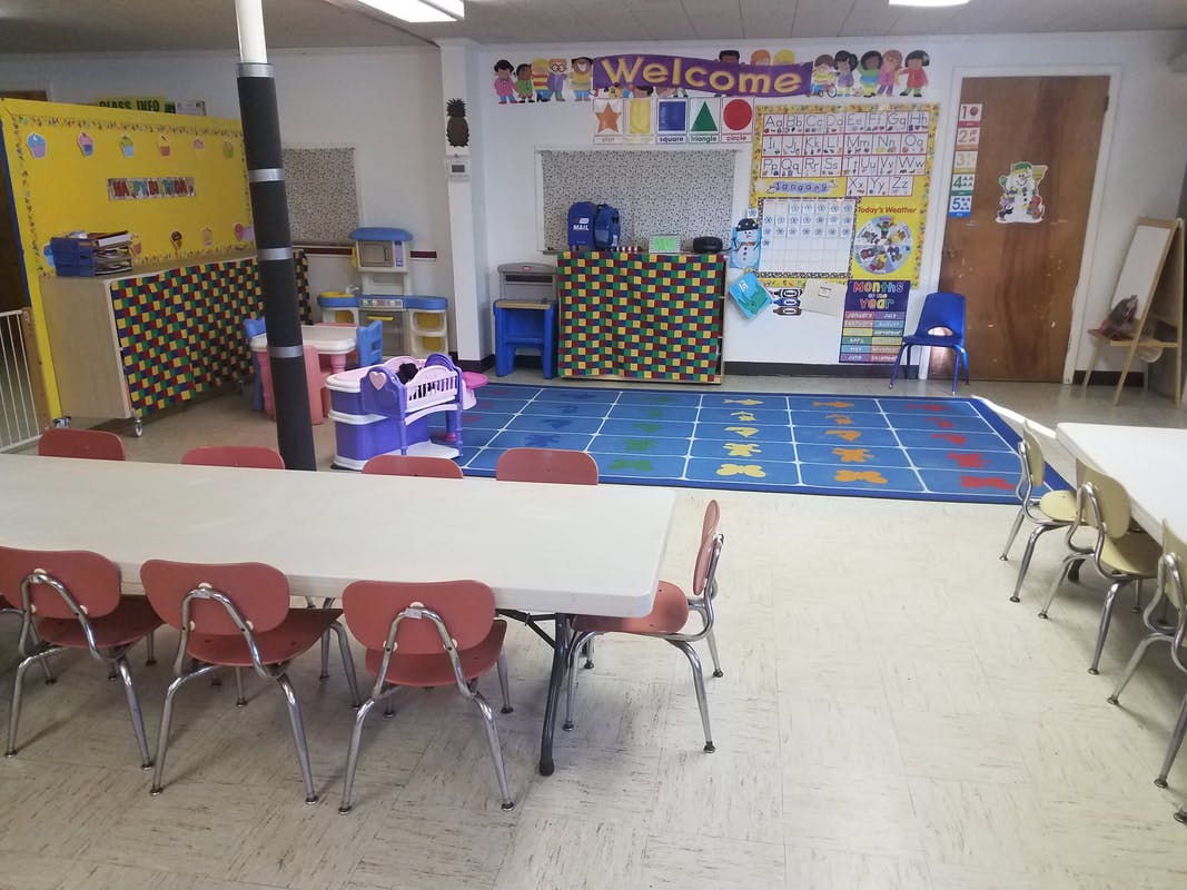 Classroom with tables and chairs, a blue rug, and a "Welcome" sign