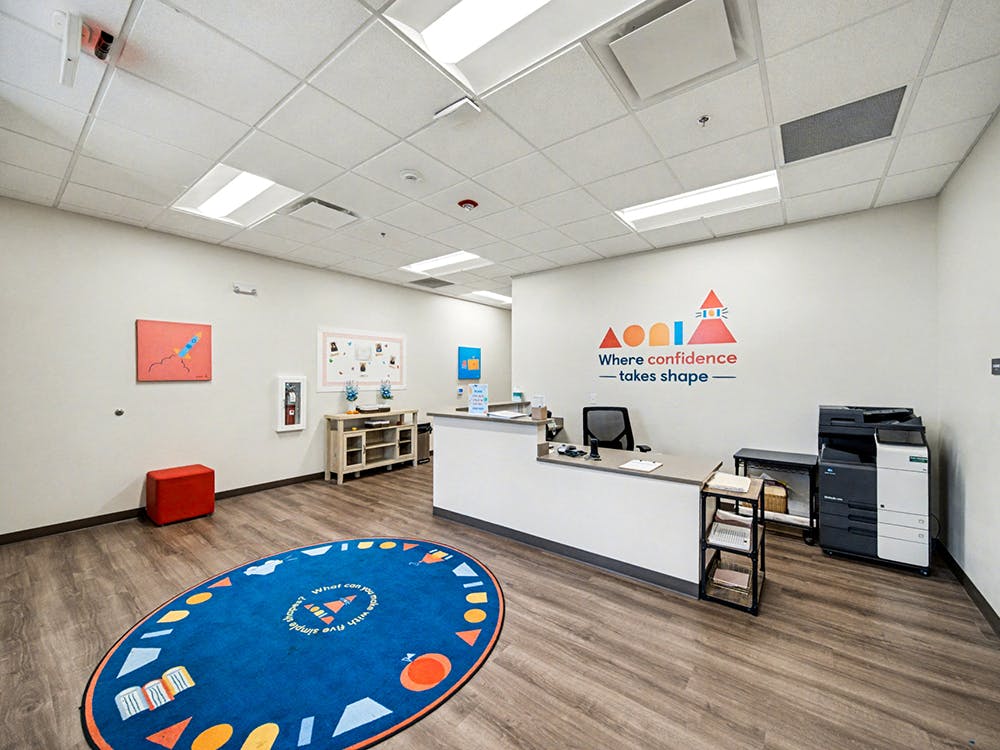 Reception desk in an office with a colorful logo on the wall and a blue rug