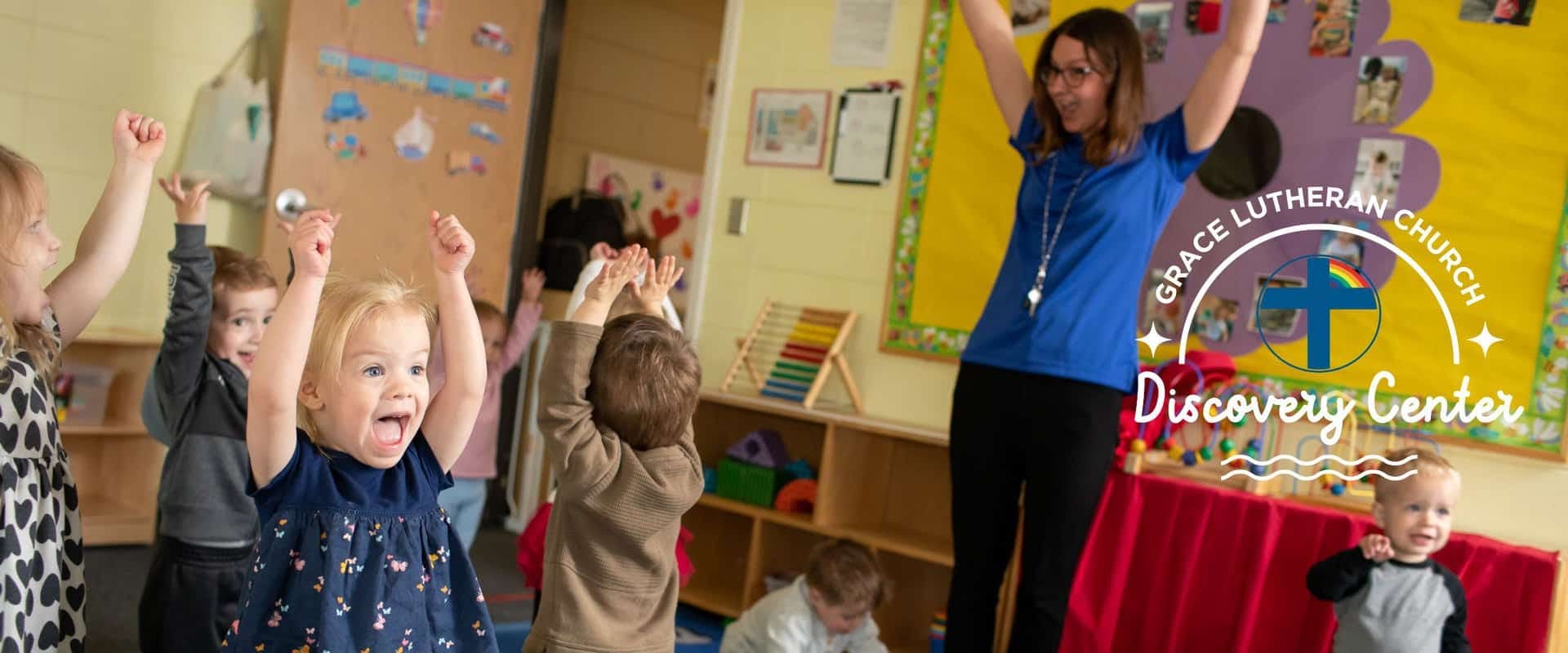 Adult and children with arms raised in a classroom