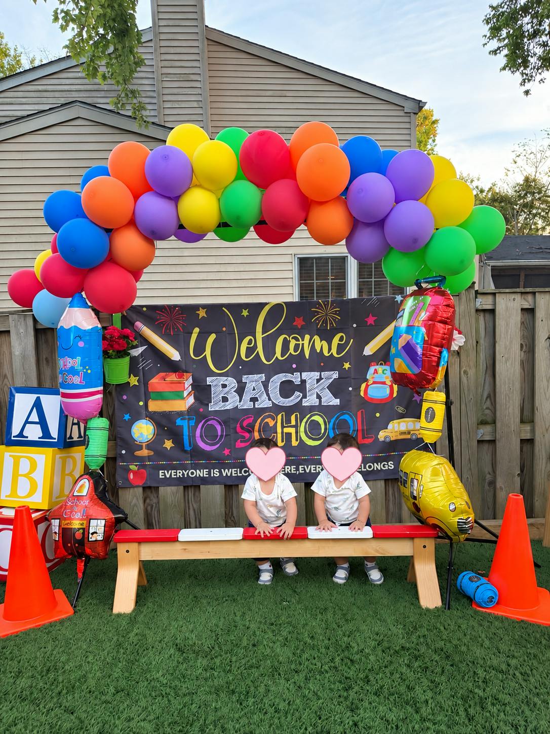 Two children sitting on a bench in front of a Welcome Back to School banner
