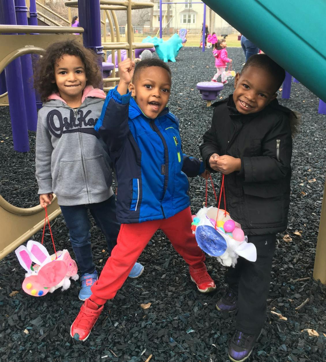 Three children holding Easter baskets on a playground