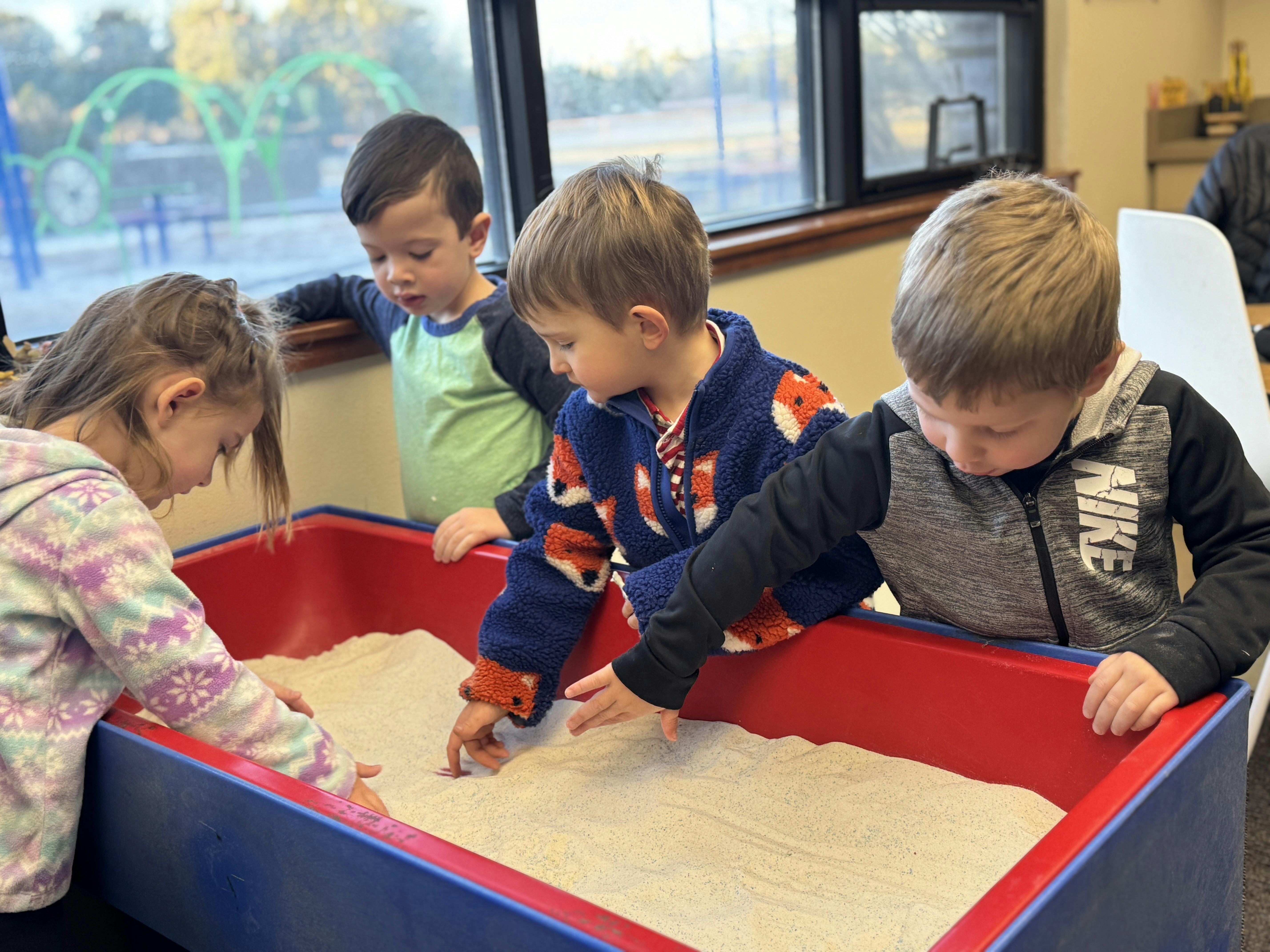 Four children playing in a sand table in a classroom