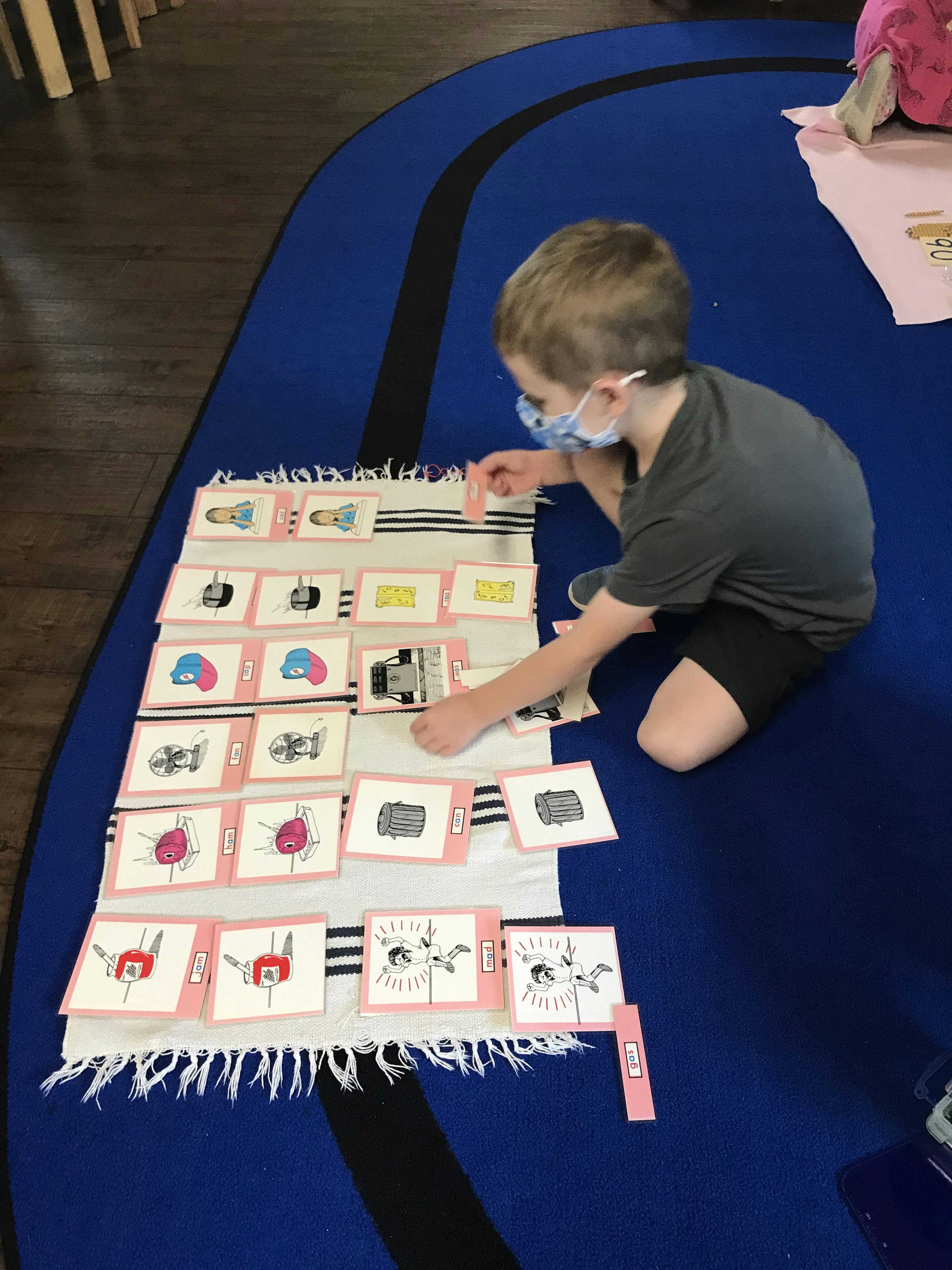 Child in a mask arranging picture cards on a rug